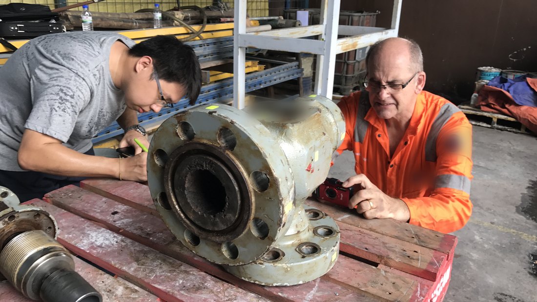 Two engineers examining a failed valve body together, one marking it up and one photographing it for the record