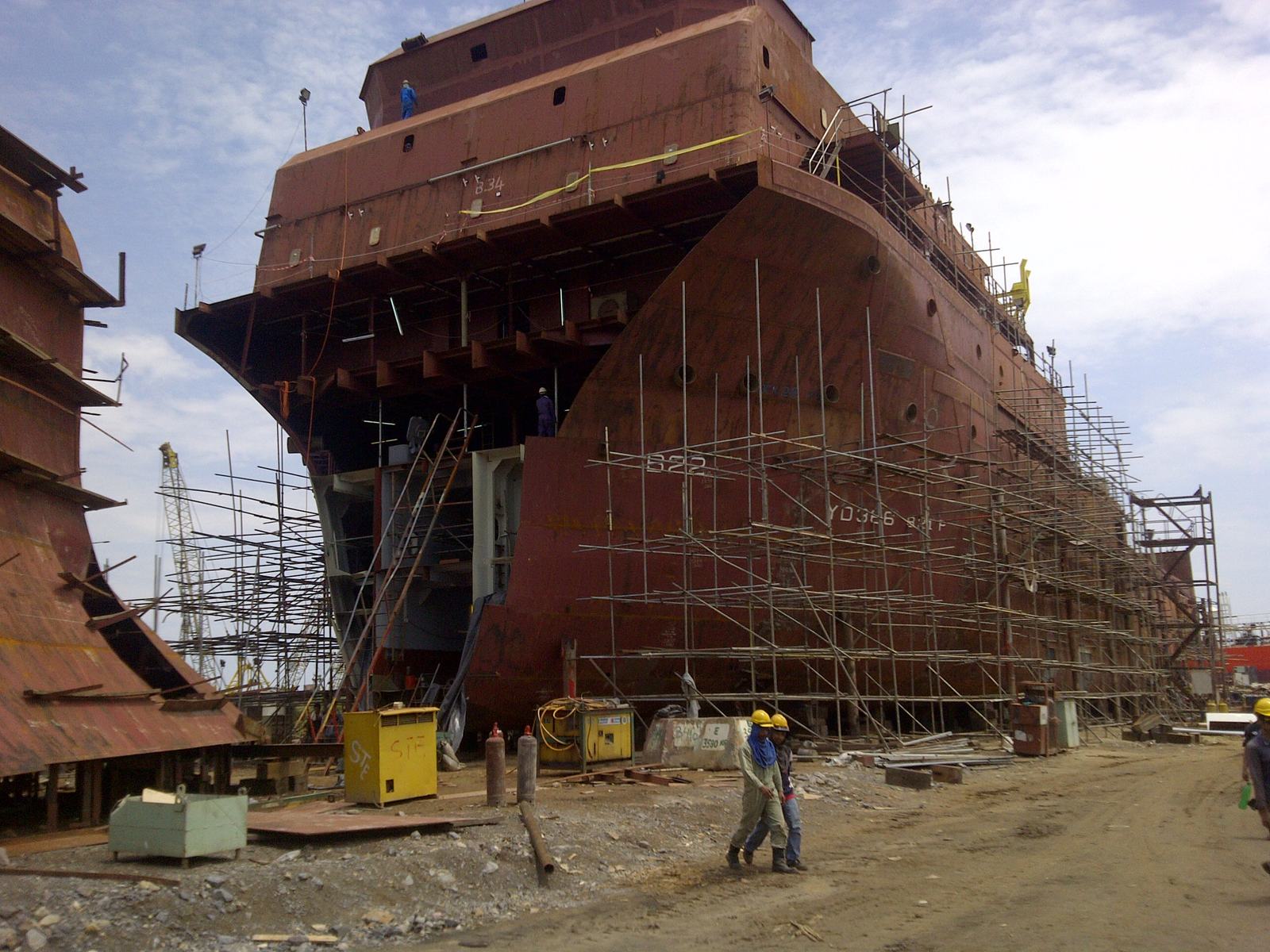 Large steel vessel under construction in a fabrication yard, surrounded by scaffolding